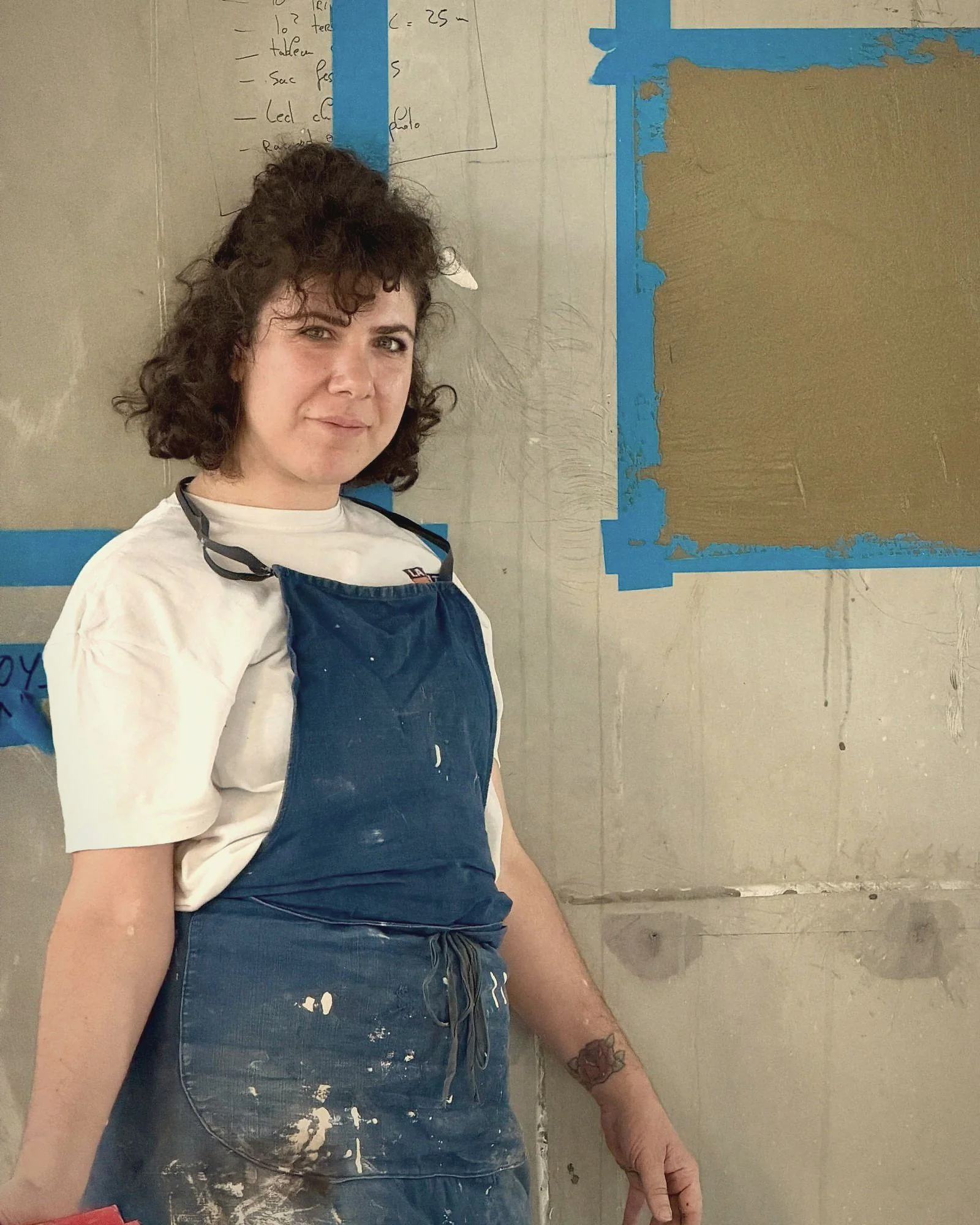 Portrait de Justine Charreyre en tablier de travail devant ses essais d’enduits ocre
