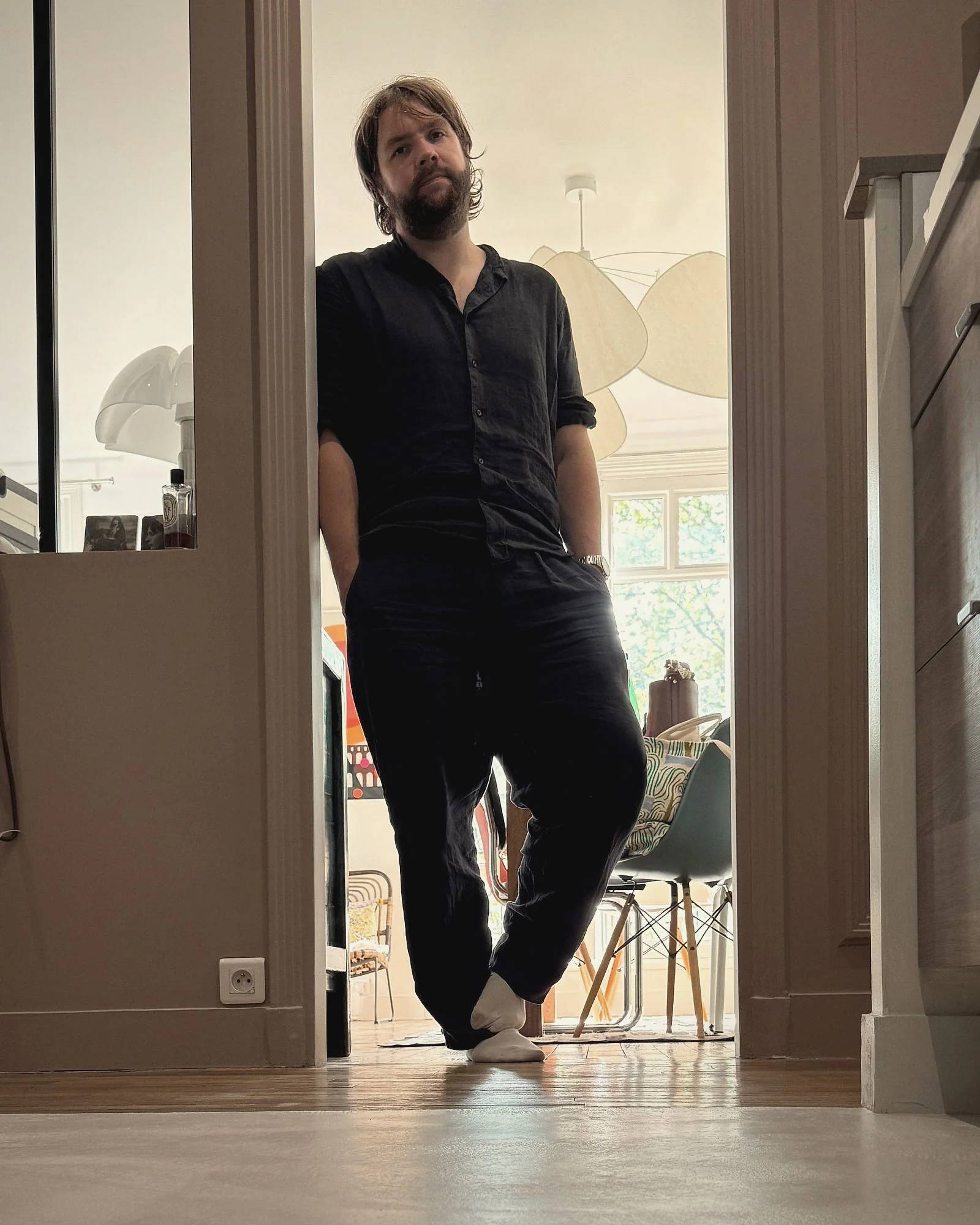 Portrait de Maxime Etchenou, en lin noir, appuyé dans l’encadrement d’une porte